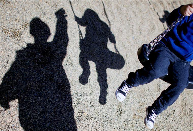Kindesunterhalt: Hierfür dürfen Eltern das Geld wirklich verwenden Eine Person steht vor einem Kind, das auf einer Schaukel sitzt. Im Hintergrund sind die Schatten zu erkennen.