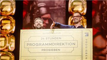 Klaas Heufer-Umlauf (l) und Joko Winterscheidt hinter einem Schild mit der Aufschrift „Gutschein für 24 Stunden Programmdirektion ProSieben“.
