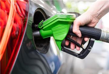 Eine Frau hält an einer Tankstelle an einer Zapfsäule eine Zapfpistole in der Hand und betankt ein Auto.
