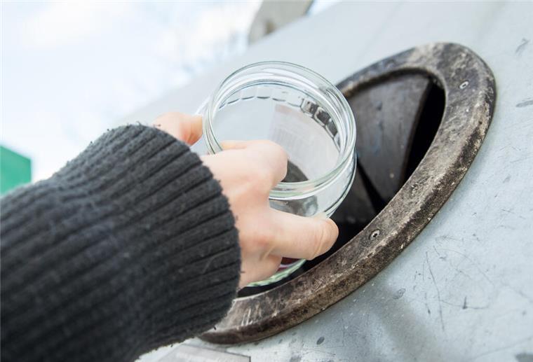 Eine Hand hält ein Konservenglas vor die Öffnung eines Altglascontainers