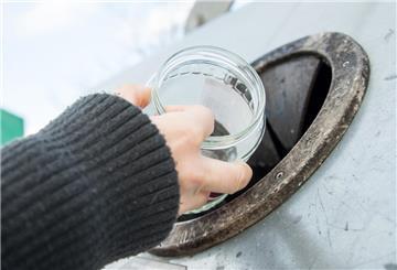 Eine Hand hält ein Konservenglas vor die Öffnung eines Altglascontainers