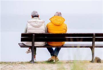 Zwei ältere Menschen sitzen auf einer Bank und schauen aufs Meer. 