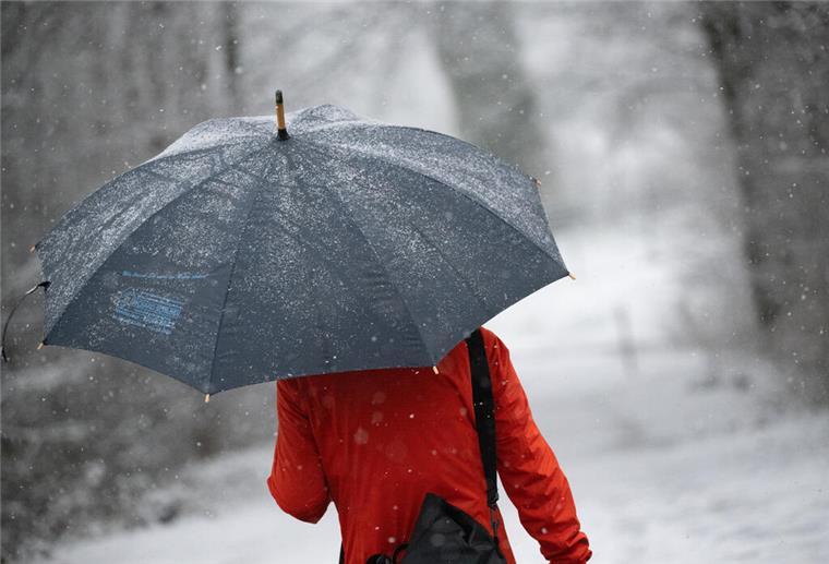  Eine Frau geht mit Regenschirm durch den Schnee. 