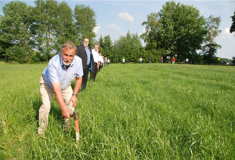 Lintig: Der erste Pflock fürs neue Feuerwehrhaus sitzt Lintigs Ortsbürgermeister Wilhelm Boldt schlägt den ersten Pflock ein fürs neue Feuerwehrhaus in Lintig. Auch Bürgermeister Thorsten Krüger (dahinter), und Mitarbeiter aus Verwaltung und Fachausschuss und Kameraden der Feuerwehr haben sich aufgestellt, um die Ausmaße des Gebäudes zu verdeutlichen.