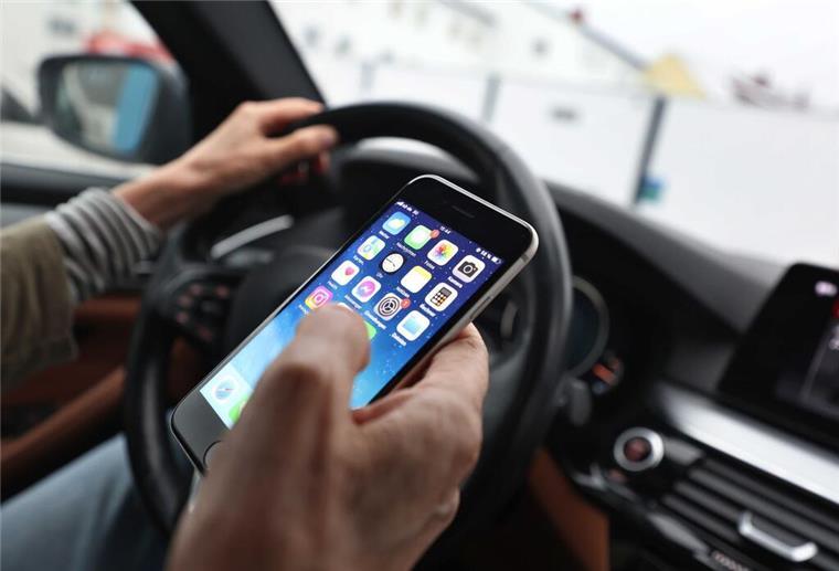 Ein Mann blickt auf sein Handy während er ein Auto fährt. 
