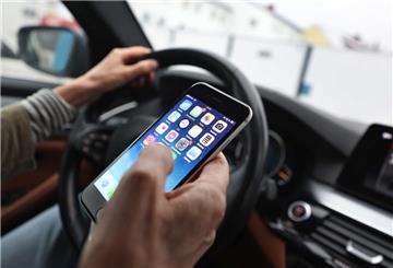 Ein Mann blickt auf sein Handy während er ein Auto fährt. 