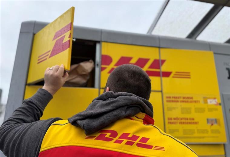 Ein Paketbote von DHL steht an einer Packstation, um diese mit Paketen zu befüllen.