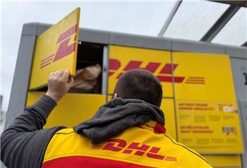 Ein Paketbote von DHL steht an einer Packstation, um diese mit Paketen zu befüllen.