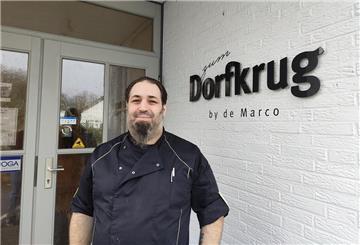 Ein Mann in Kochkleidung steht vor einem Restaurant.