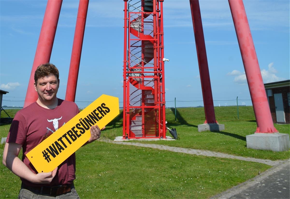 Marketingexperte Oliver Knagge weist mit dem „Watt Besünners“-Schild auf das Leuchtfeuer. Foto: Timmermann