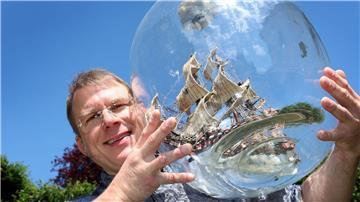 Matthias Schultz hält ein von ihm gebautes 40 Zentimeter hohes und 38 Zentimeter langes Buddelschiff welches in einem 50 Liter fassenden Gärballon hängt.