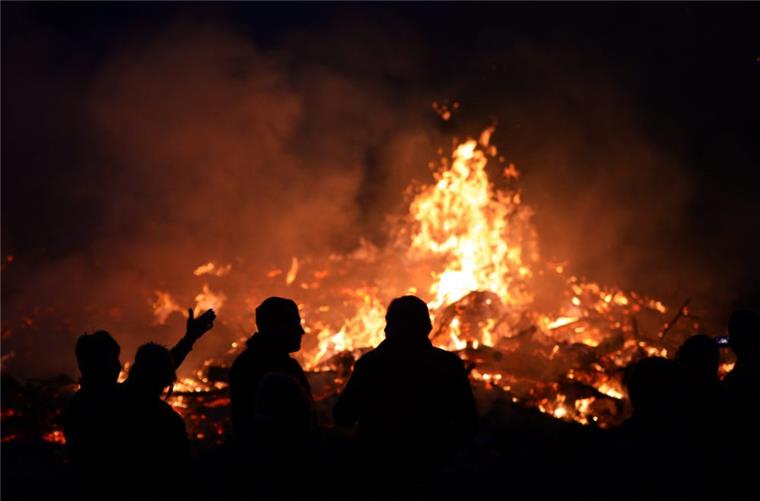 Menschen stehen am an einem Osterfeuer. Angesichts der hohen Waldbrandgefahr hat der Beauftragte des Landes zu besonderer Vorsicht bei den traditionellen Osterfeuern gemahnt.