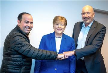 zwei Männer mit der Wachsfigur von Frau Merkel.