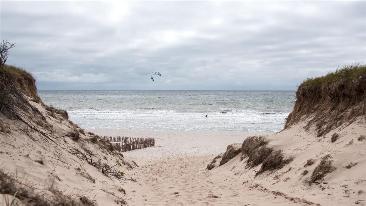 Ein Kitesurfer ist auf der Nordseeinsel am Strand von Rantum auf der Nordsee unterwegs, über der dunkle Wolken hängen.