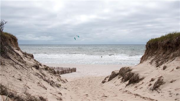Ein Kitesurfer ist auf der Nordseeinsel am Strand von Rantum auf der Nordsee unterwegs, über der dunkle Wolken hängen.