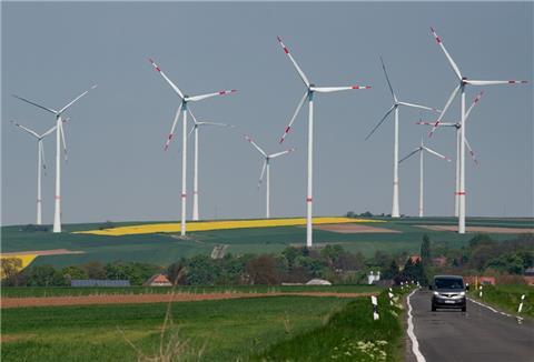Windräder sind hinter einer Landstraße zu sehen. Entlang der Autobahn A63 stehen mehrere Windkraftanlagen. 