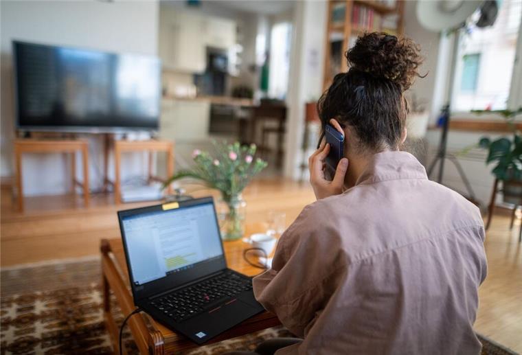 Eine Frau telefoniert und sitzt vor ihrem Laptop.