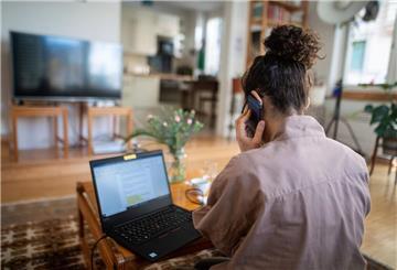 Eine Frau telefoniert und sitzt vor ihrem Laptop.