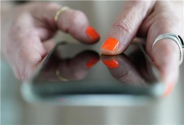 Eine Frau mit orangefarbenem Nagellack hält ein Handy in der Hand.