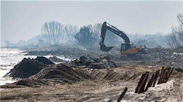 Mit einem Bagger werden große Steine am Strand am Hafen von Damp verladen.