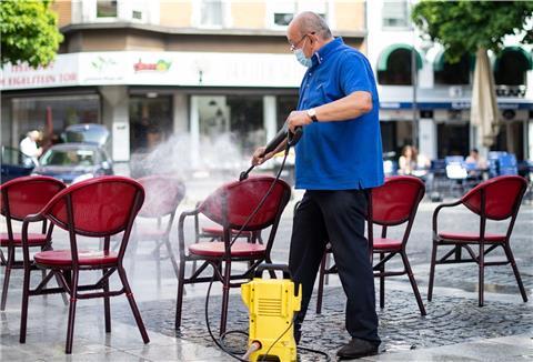 Mit einem Hochdruckreiniger säubert ein Gastronom die Stühle seines Cafes.
