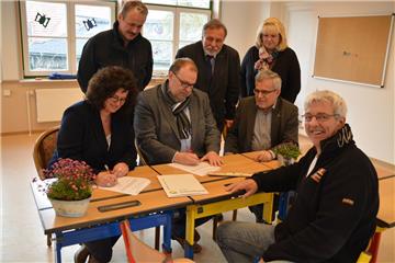 Mit ihren Unterschriften besiegeln Karina Kramer (sitzend von links) und Thorsten Krüger die Vereinbarung zur Nutzung der Lintiger Schulräume als Außenstelle der Schule am Wiesendamm. Zum feierlichen Anlass dürfen auch Erster Stadtrat Jürgen Zehm und Schulleiter Thomas Kroll nicht fehlen. Als weitere Vertreter der Verwaltung sind Thorsten Gerken (hinten von links), Wilhelm Boldt und Iris Dittmann im Klassenraum dabei. Foto Scheiter