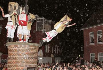Mit Masken verkleidete Männer des Vereins Borkumer Jungens stürzen sich am Abend (Aufnahme vom 05.12.2011) beim traditionellen Klaasohm-Fest von einem Podest.