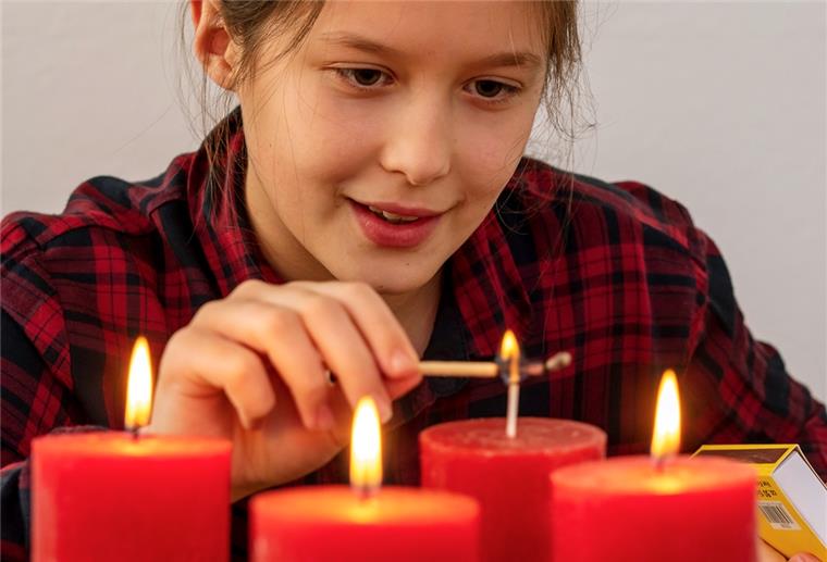 Vorsicht vor Verbrennungen: Mädchen zündet Adventskerzen an.