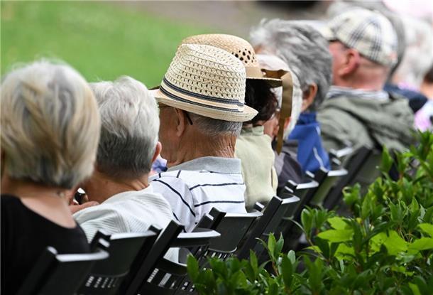 Ältere Menschen besuchen in einem Kurpark das Konzert eines Schulorchesters.