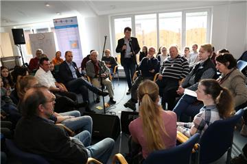 Moderator Carsten Bunk (stehend) diskutiert mit Schülern, Politikern, Rathaus-Mitarbeitern und weiteren Experten über Zukunftsfragen.