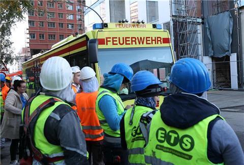  Einsatzfahrzeuge der Feuerwehr und Bauarbeiter stehen vor einer Baustelle. 