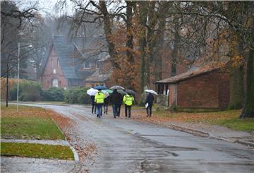 Männer mit Regenschirmen gehen eine Dorfstraße entlang