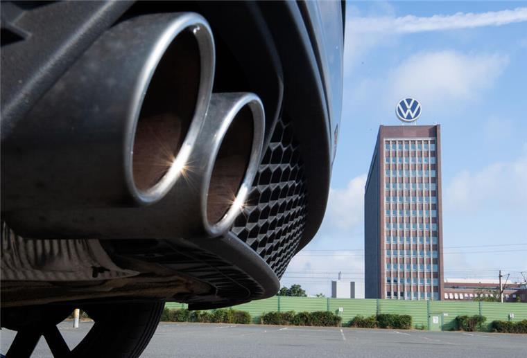 Auspuffrohre eines Volkswagens fotografiert mit dem Markenhochhaus am VW Werk Wolfsburg.