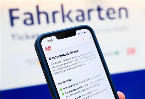  Eine Person hält am Hauptbahnhof ein Smartphone in der Hand, auf dessen Display eine Information zum Kauf des Deutschlandtickets zu sehen ist, während sie vor einem Fahrkartenautomaten steht. 