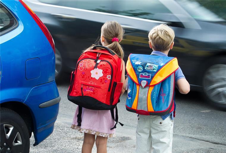 Zwei Schulkinder an einer Straße mit Autos.