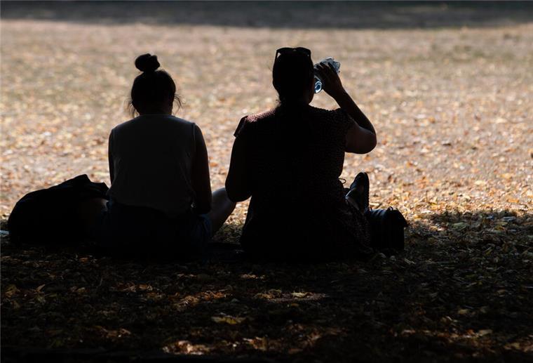 Es bleibt heiß in vielen Teilen Deutschlands Zwei Frauen sitzen in einem Park im Schatten der Bäume, um sich vor der Hitze zu schützen. Eine von ihnen trinkt aus einer Wasserflasche.