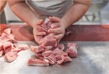 Ein junger Metzger hält geschnittenes Schweinefleisch in der Hand.