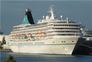 Das Kreuzfahrtschiff „Artania“ liegt im Hafen. Das weiße Schiff mit türkisfarbenen Details verfügt über mehrere Decks, auf denen Rettungsboote zu sehen sind. Der markante Schornstein trägt das Logo von Phoenix Reisen.