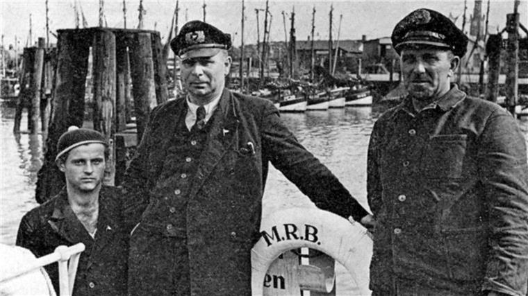 Schwarz-Weiß-Aufnahme von drei Männern an Bord eines Schiffes im Hafen. 