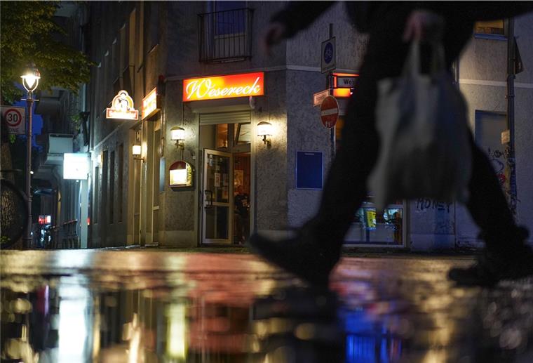 Wegen Corona: Berlin beschließt Sperrstunde Person läuft abends auf einer Straße. Im Hintergrund eine Kneipe.