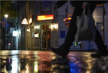 Person läuft abends auf einer Straße. Im Hintergrund eine Kneipe.