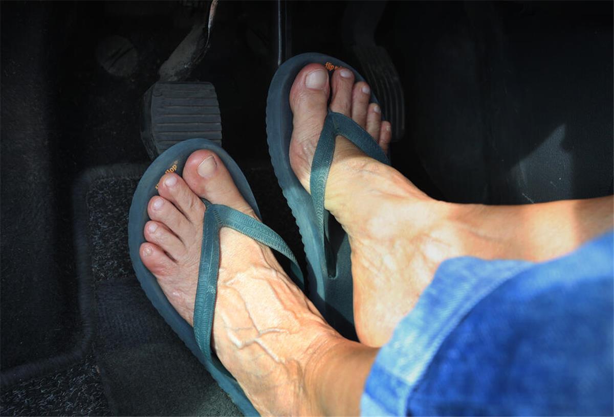 Mit Flip-Flops oder barfuß Autofahren: Was erlaubt ist – und wann es teuer wird Ein Mann trägt Flip-Flops und fährt Auto.