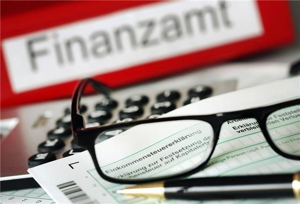 Auf einem Vordruck für die Steuererklärung liegt vor dem Aktenordner mit dem Aufdruck „Finanzamt“ ein Stift und eine Brille.