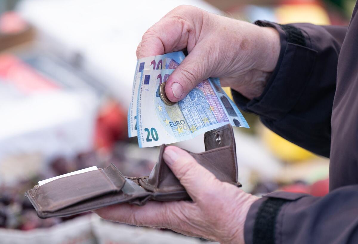 Eine Frau sortiert auf einem Wochenmarkt das Wechselgeld für ihre Einkäufe in ein Portemonnaie. 