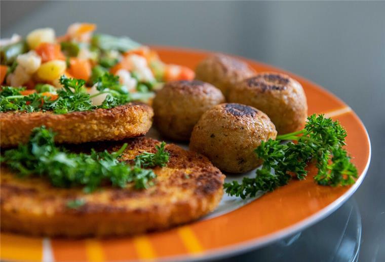 Falafel, vegane Schnitzel und Gemüse liegen auf einem Teller in einer Küche.