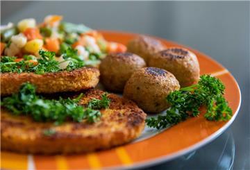 Falafel, vegane Schnitzel und Gemüse liegen auf einem Teller in einer Küche.