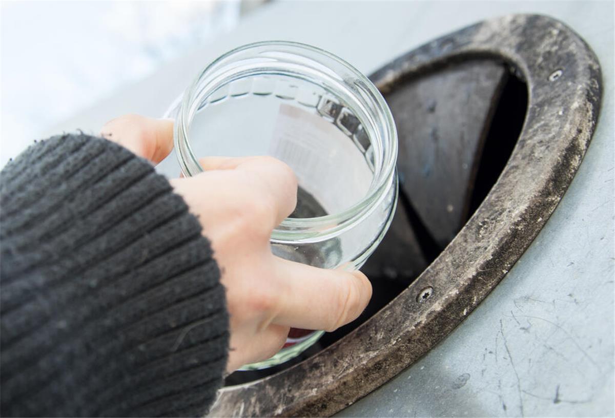 Abfall-Irrtum beim Glasrecycling! Nicht alles gehört in den Altglascontainer Eine Hand, die ein Glas ohne Deckel in einen Altglas-Container schmeißt.