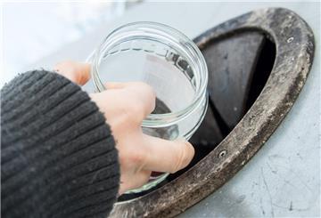 Eine Hand, die ein Glas ohne Deckel in einen Altglas-Container schmeißt.
