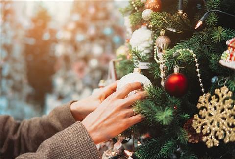 Frau hängt Weihnachtskugeln an einen Tannenbaum.
