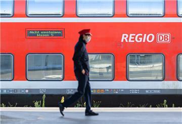 Ein Mitarbeiter der Deutschen Bahn (DB) läuft auf einem Bahnsteig und ein Zug der DB Regio steht auf einem Gleis dahinter